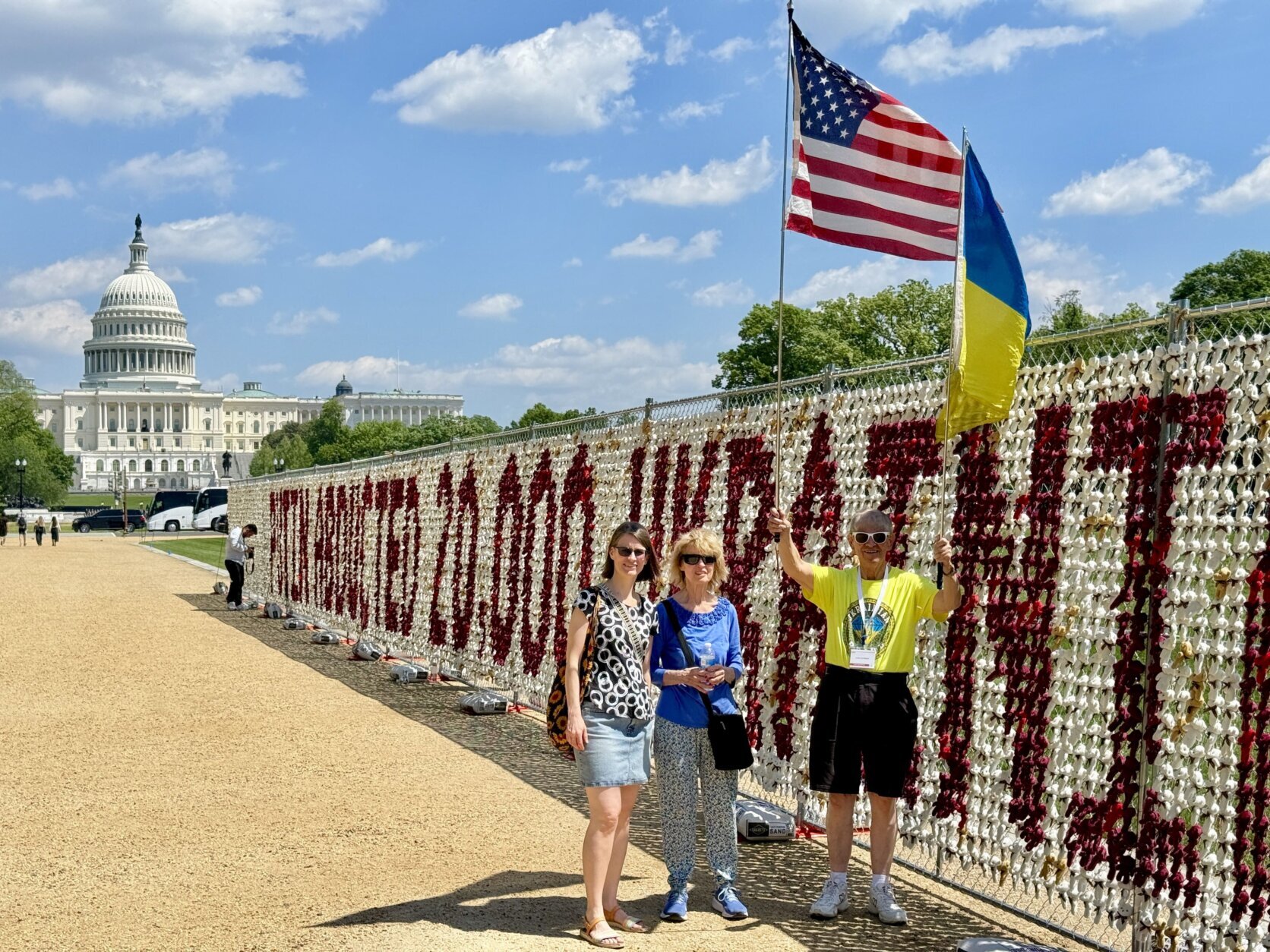 people stand on national mall with capitol building in background in front of large message made of teddy bears holding american and ukrainian flags