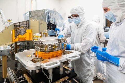 scientists in white suits and gloves work on space technology in a lab