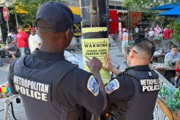 Washington DC Metropolitan Police officers place signage on a light pole informing the public that the area near the Nationals Park is under designate targeted juvenile curfew zone for youth under the age of 18, Friday. April 17, 2026 in Washington. (AP Photo/Pablo Martinez Monsivais)
