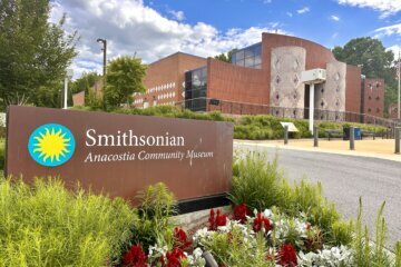 a sign at the driveway of the Anacostia Community Museum, with the building itself in the background.