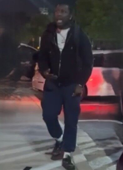 Man wearing black hoodie, white under shirt, and blue pants. He is talking to someone off camera