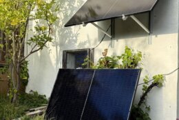 A pair of plug-in solar panels leaning against a house's stone wall, beneath another plug-in panel.
