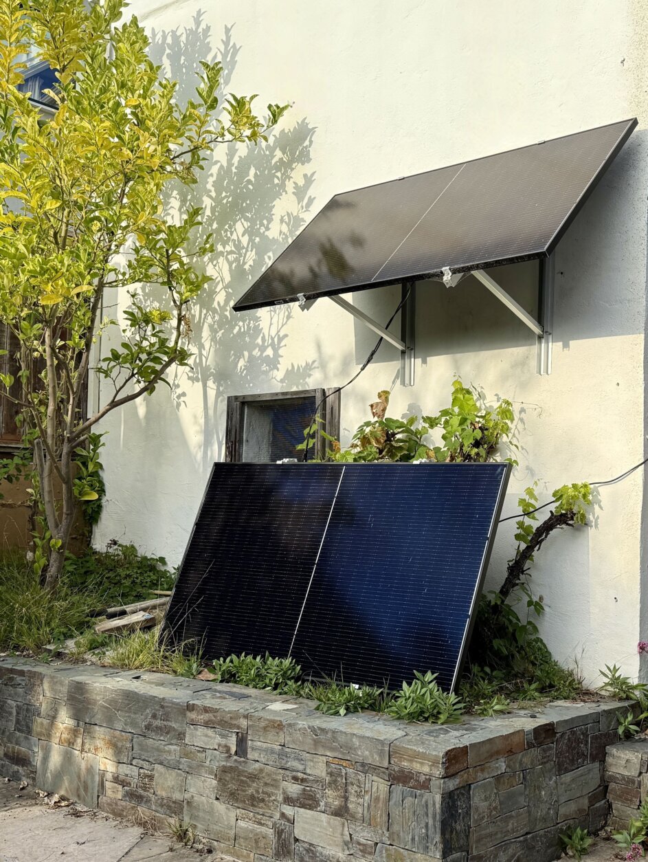 A pair of plug-in solar panels leaning against a house's stone wall, beneath another plug-in panel.