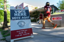 A football player walks by a "vote here vote aqui" sign