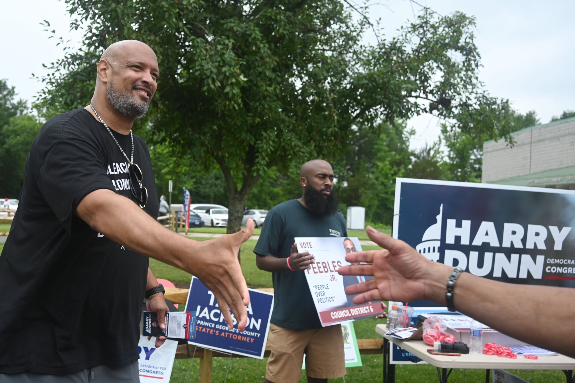 man reaches for handshake at polling place on election day with campaign signs behind