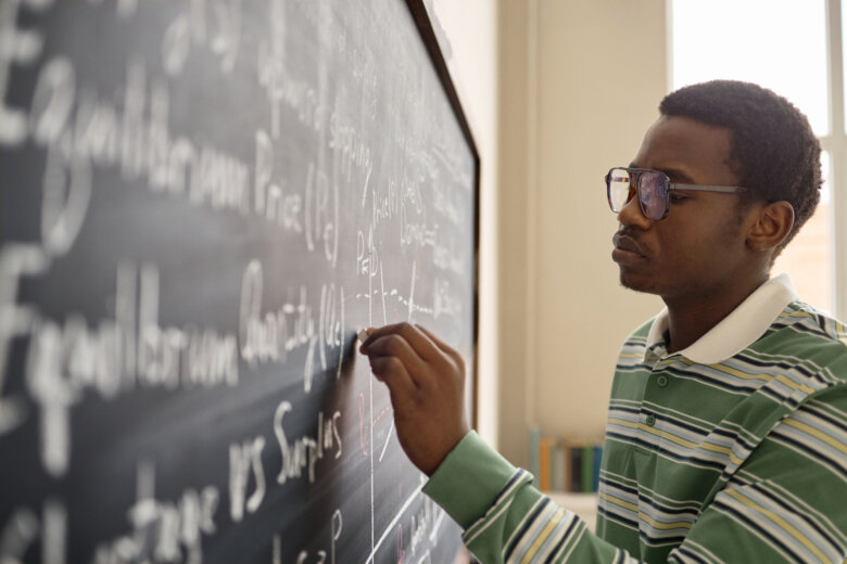 Black male teenager solving math equations on classroom chalkboard