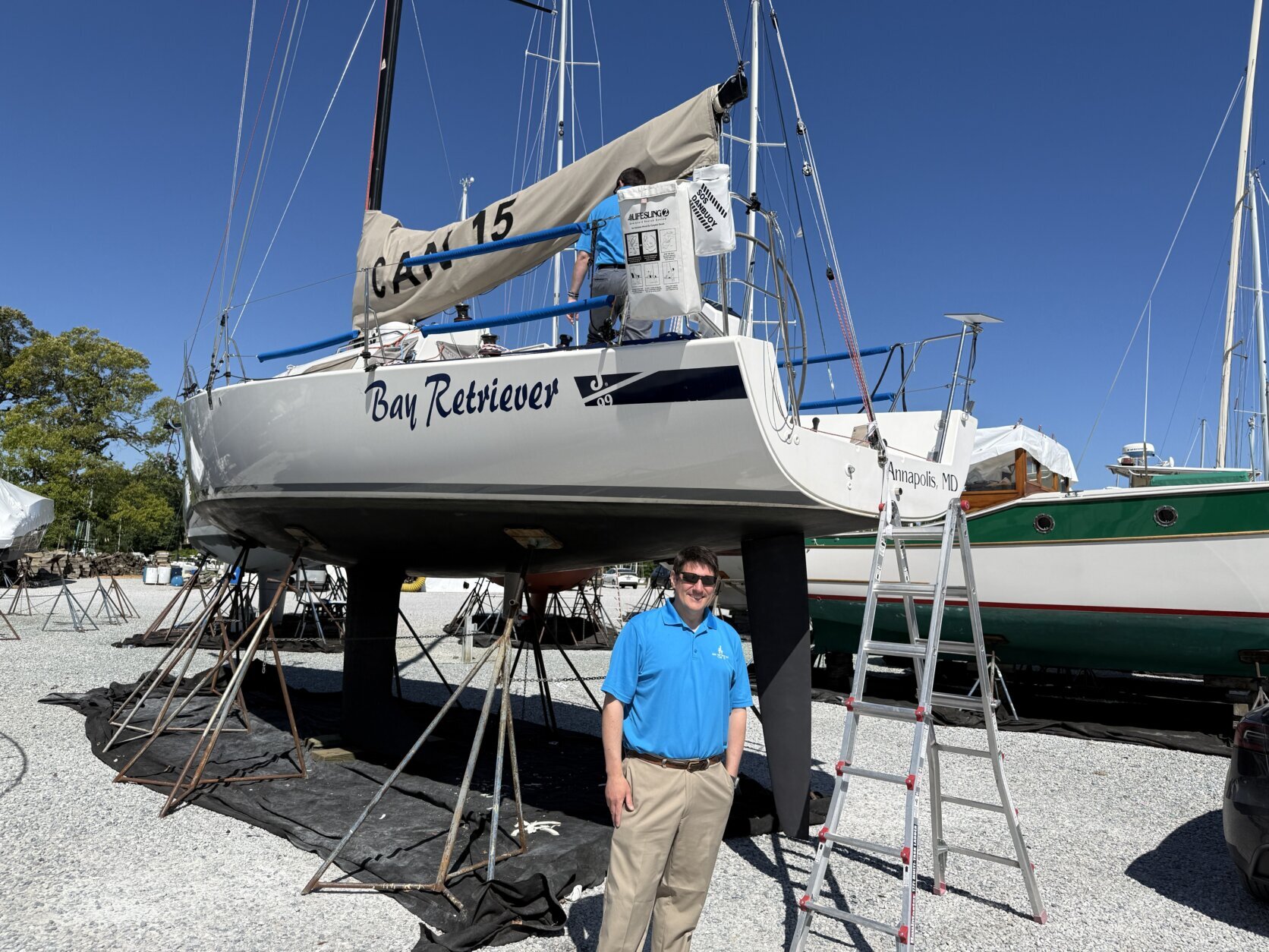 a man in a blue polo stands beneath a large sailboat
