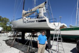 a man in a blue polo stands beneath a large sailboat