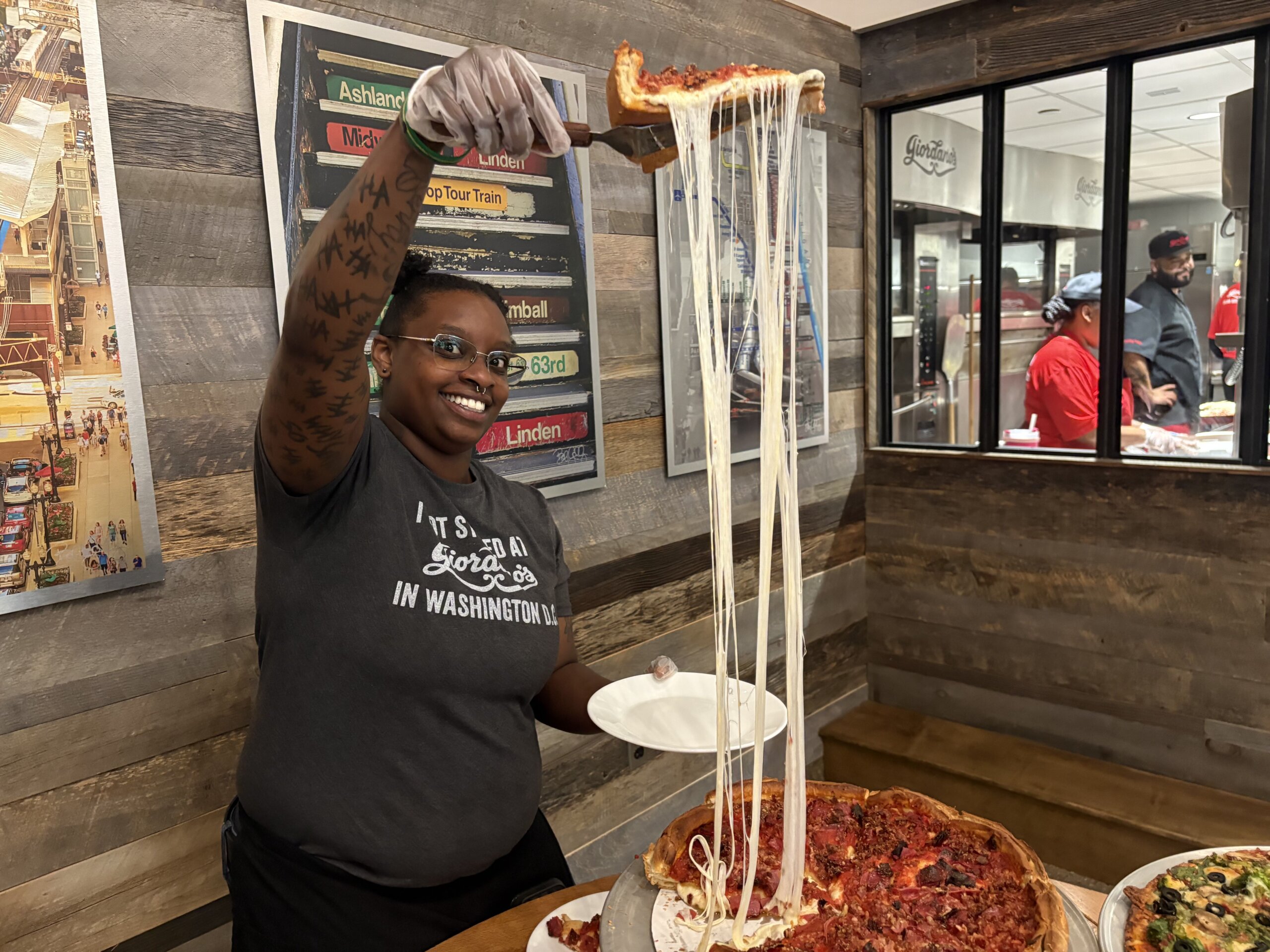 A server holds a slice of pizza aloft over a whole pie, with cheese stretching in between