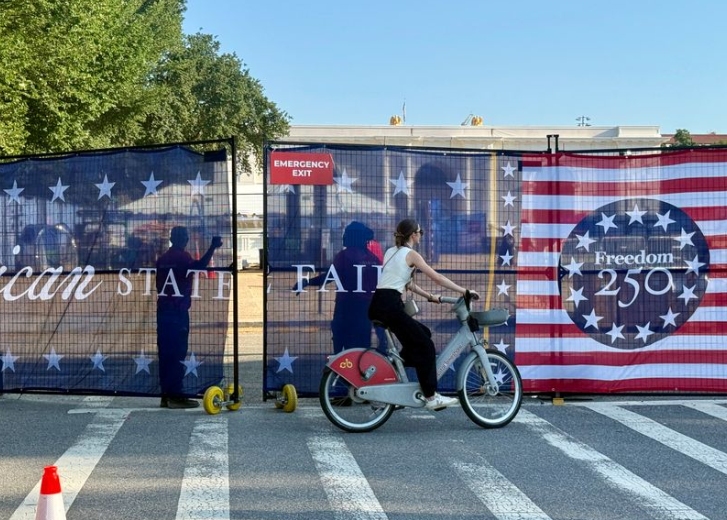 woman on bike passing America 250 sign on the Mall