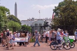 Independence Day holiday visitors endure sweltering temperatures as they try to get a view of the White House beyond metal fencing surrounding Lafayette Park, in Washington, Friday, July 3, 2026. (AP Photo/J. Scott Applewhite)
