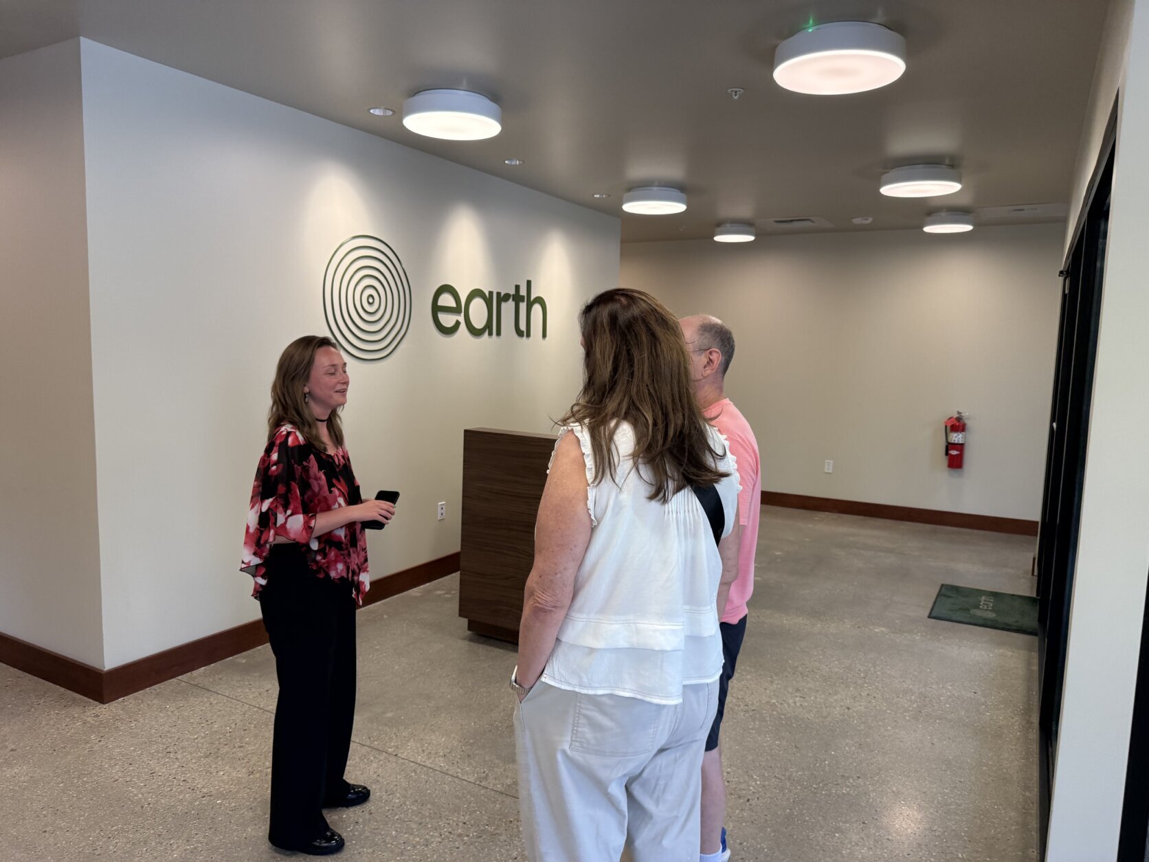 A person stands talking to two other people in the apparent front room of a human-composting facility.