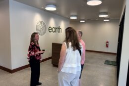 A person stands talking to two other people in the apparent front room of a human-composting facility.