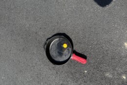 An uncooked egg in a cast-iron pan atop an asphalt driveway.