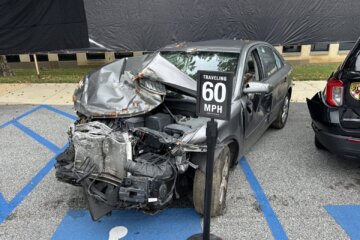 Car with front end crushed with sign indicating it was damaged in a 60 mph crash