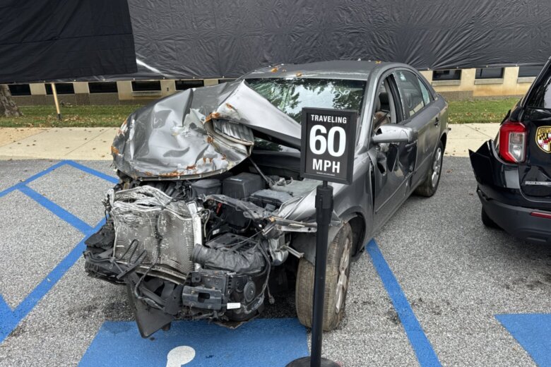 Car with front end crushed with sign indicating it was damaged in a 60 mph crash