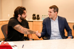 baseball player in street clothes on left shakes hand with business executive in room after signing contract