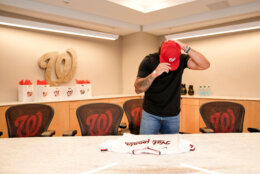 baseball player in street cloths bends head down while putting on ball cap