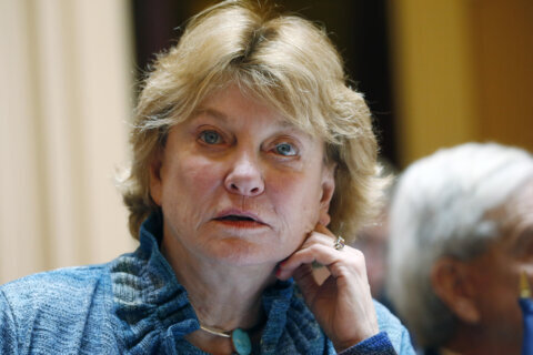 woman pictured from shoulders up leaning head on hand during legislative proceedings