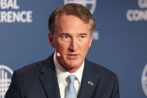 man pictured from chest up wearing suit with microphone attached to ear