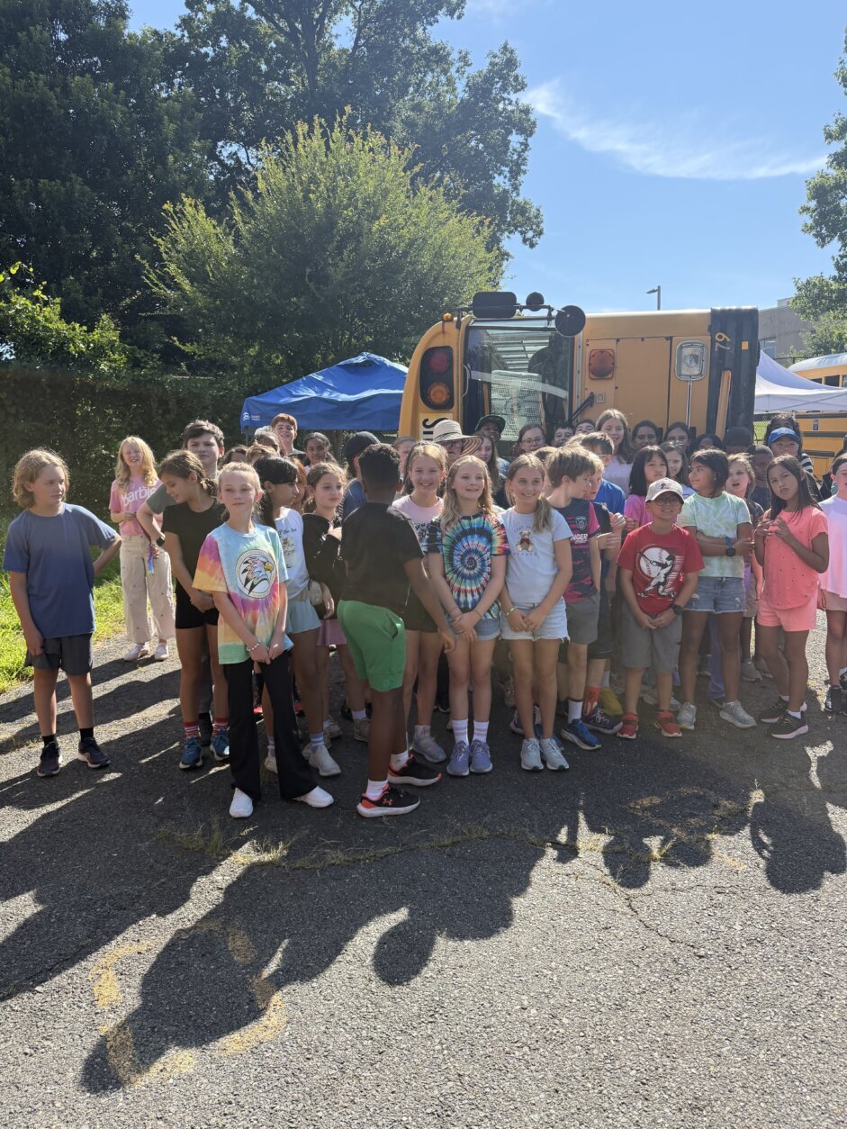 group of students pose for photo in front of overturned school bus