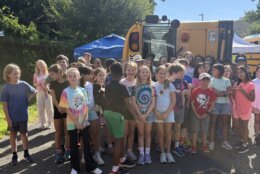 group of students pose for photo in front of overturned school bus