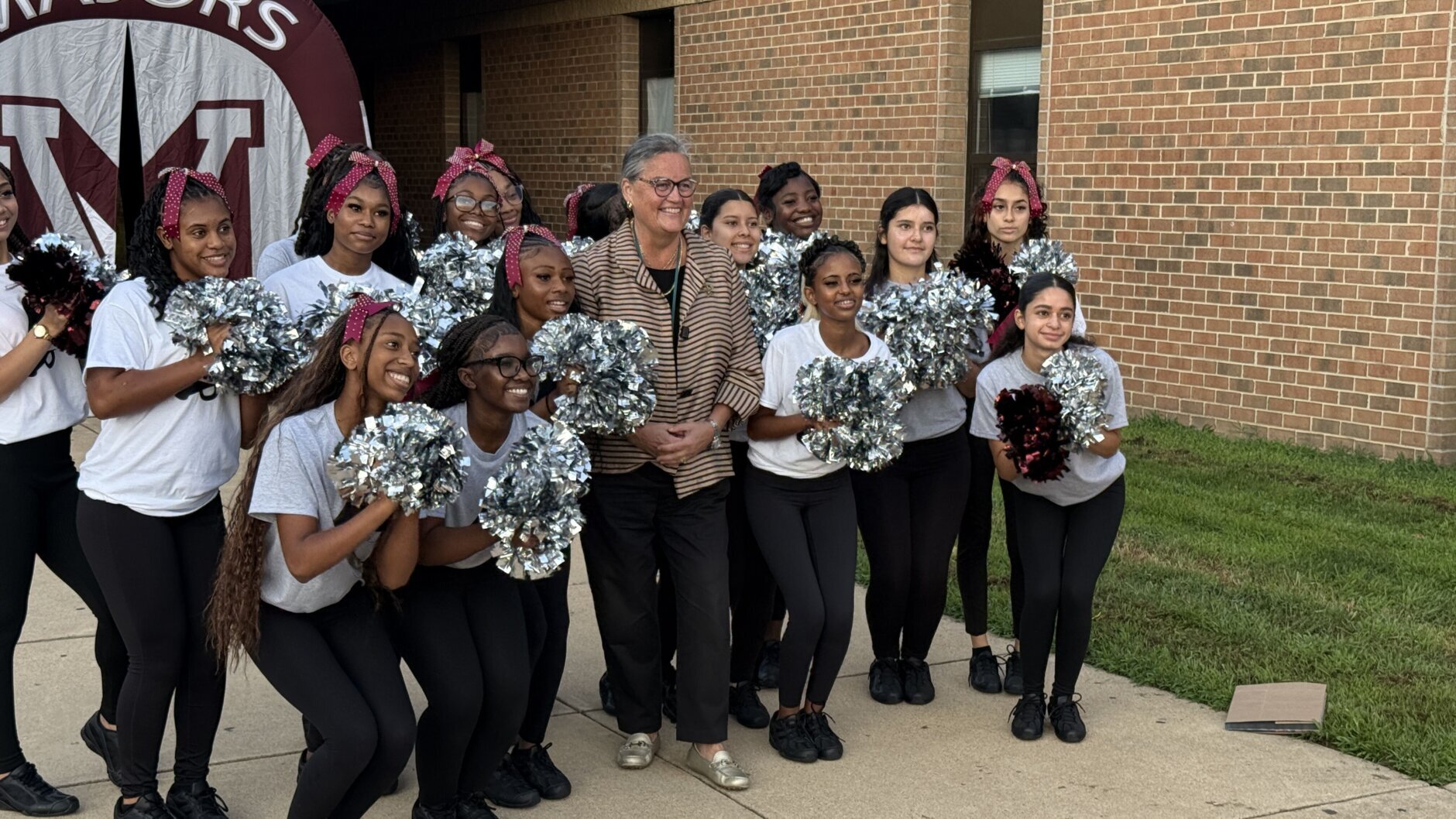 cheer leaders pose in group photo with a school official